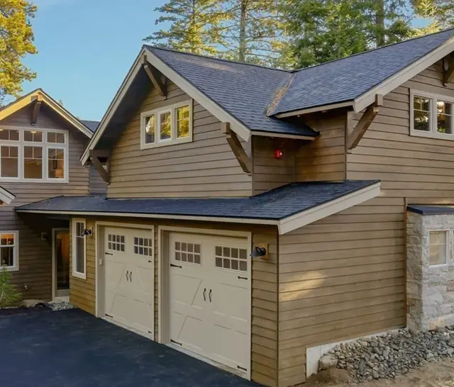 Two almond carriage doors with window tops under a gabled bonus room on a craftsman home