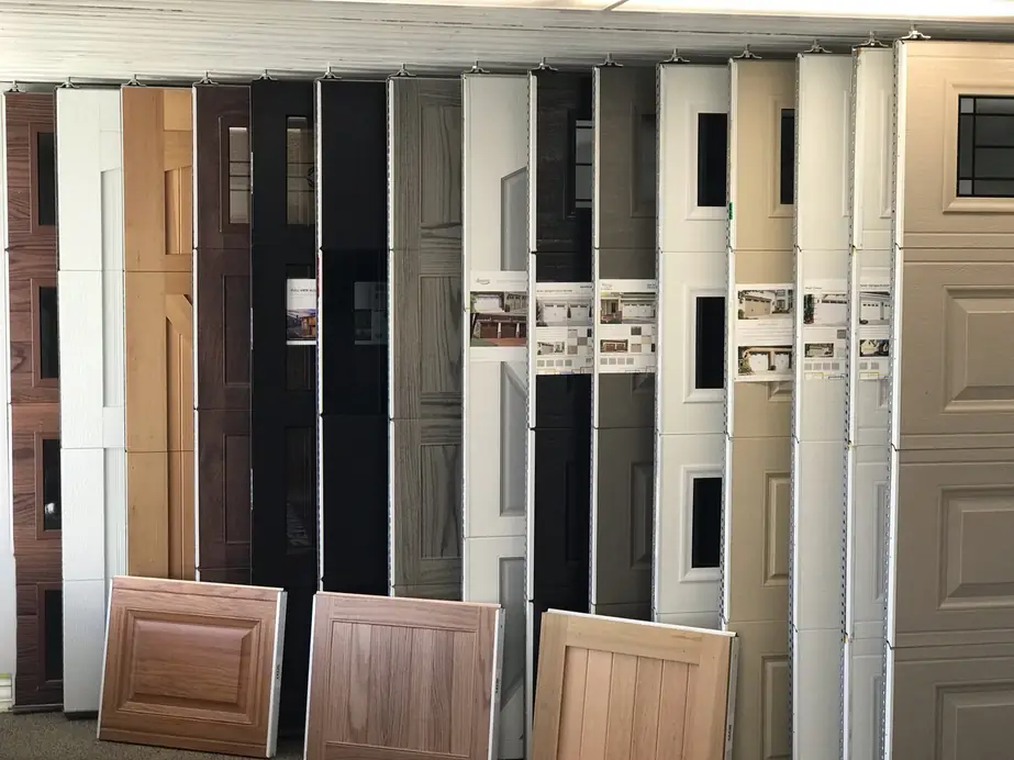 The SCI Door showroom wall: full-height garage door sections in wood-grain, black, white and tan with raised-panel samples in front