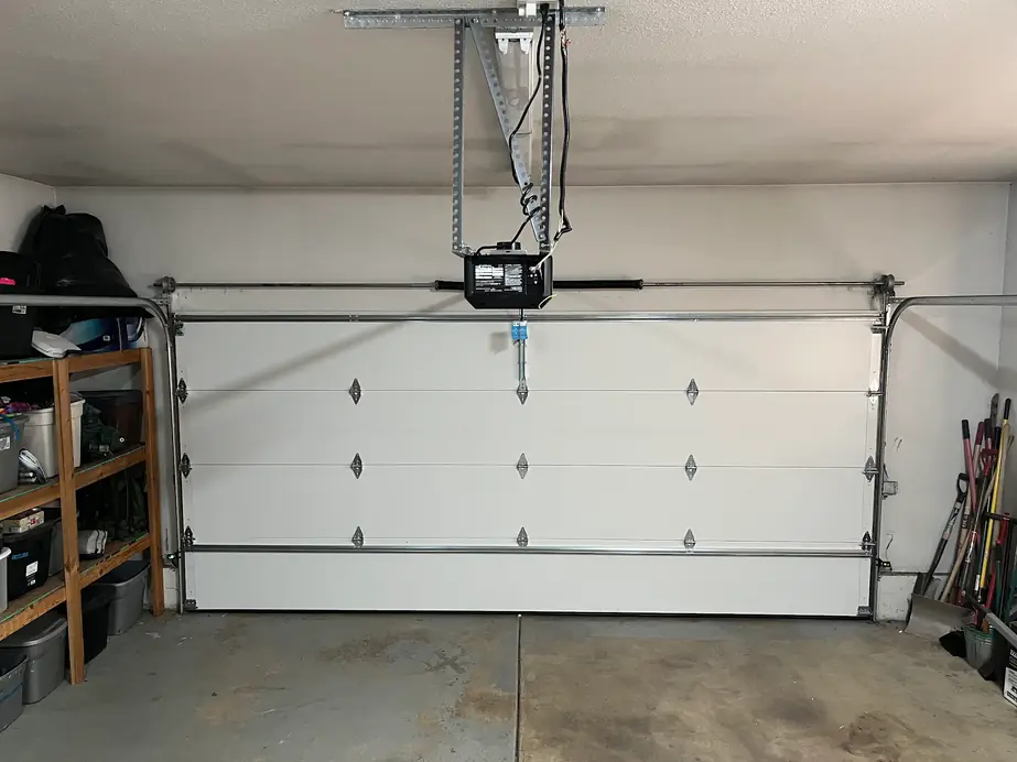 Inside a garage: a white insulated door closed under its opener rail and track