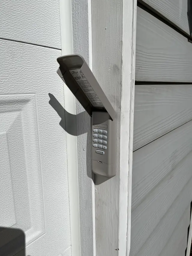 A wireless garage door keypad mounted on the door jamb with its cover open